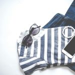 Flat lay image featuring sunglasses, striped top, jeans, and smartphone, ideal for fashion and lifestyle themes.